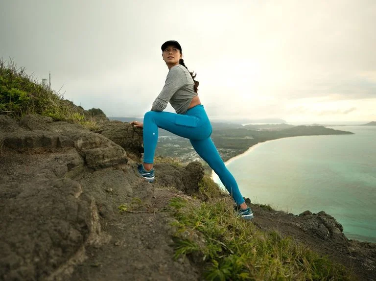 A lady climbing a mountain beside the sea in blue 3/4 leggings